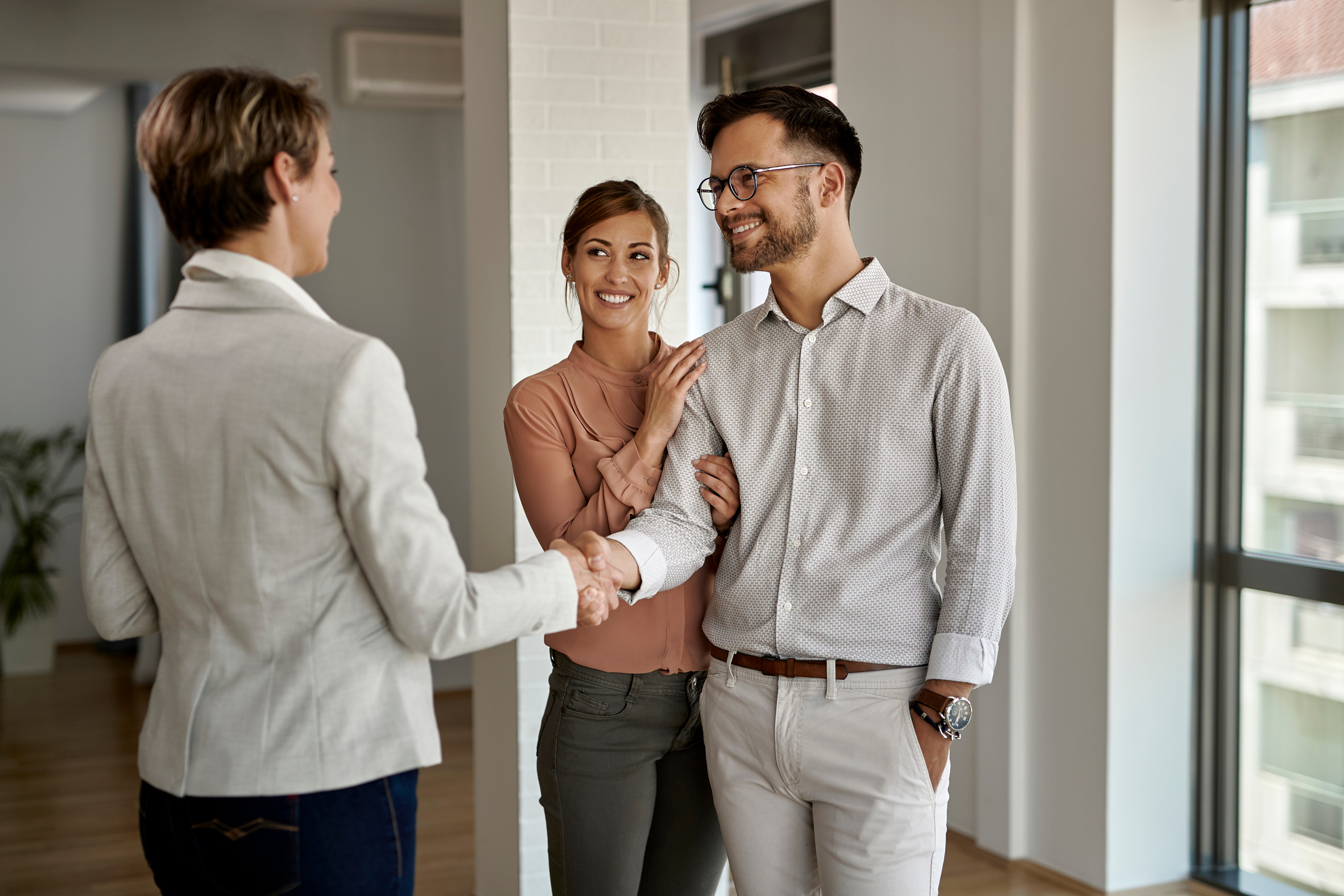 Young happy couple shaking hands with real estate agent.